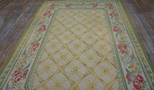 Pale floral rug with yellow trellis pattern and pink rose border lies on gray, distressed hardwood floor.