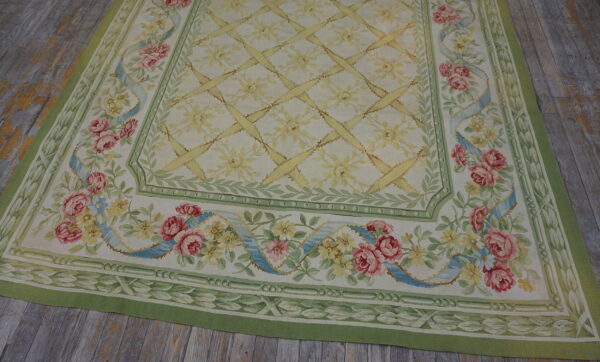 Flat woven cream rug with pink roses, a green foliage border, and a yellow trellis lying on wood floorboards.