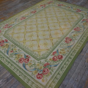 Green-bordered tapestry rug with pink roses and a yellow trellis pattern on rustic wooden flooring.