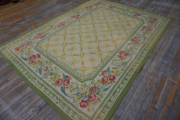 Green-bordered tapestry rug with pink roses and a yellow trellis pattern on rustic wooden flooring.