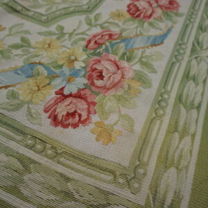 Flatweave rug corner with pink roses, yellow florals, and sage green borders on rustic wood planks.