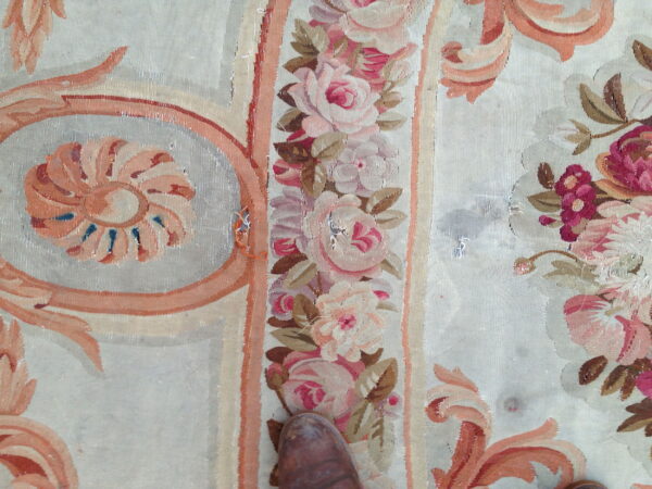 Close-up of a floral flatweave rug showing pink roses, peach scrolls, and a pale neutral background with a brown shoe toe.