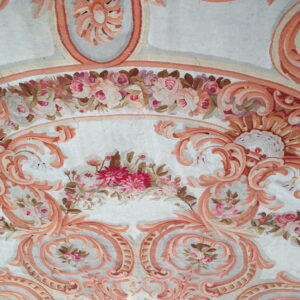 Ornate low-pile rug with salmon neoclassical scrolls and multi-colored pink floral bouquets on a pale background.