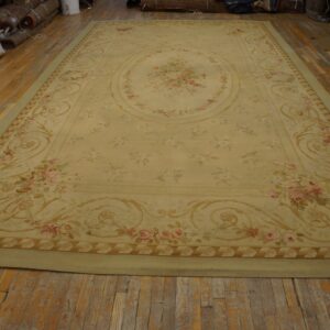 Pale yellow low-pile rug featuring a pink floral medallion and ornate border on distressed wood planks.