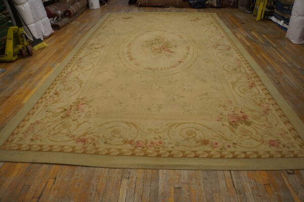 Pale yellow low-pile rug featuring a pink floral medallion and ornate border on distressed wood planks.