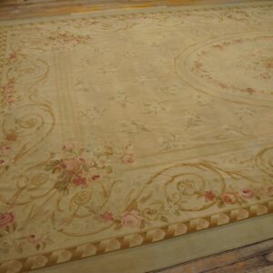Large pale yellow rug with pink floral bouquets and gold scrollwork on distressed wooden plank flooring.