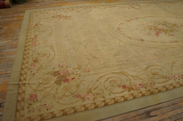 Large pale yellow rug with pink floral bouquets and gold scrollwork on distressed wooden plank flooring.