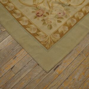 Flatweave rug corner featuring beige, pink, and olive floral motifs with a wide sage green border on weathered wood.
