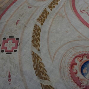 Flatweave rug detail featuring curvilinear patterns in pink, blue, brown, and white on wood flooring.