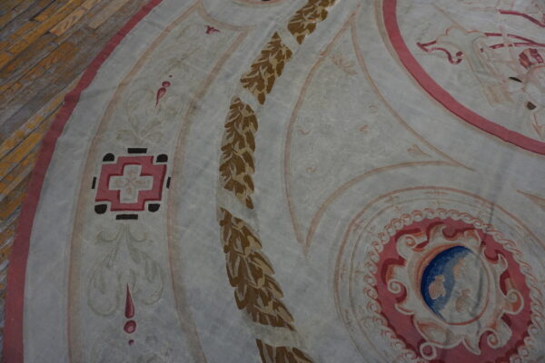 Flatweave rug detail featuring curvilinear patterns in pink, blue, brown, and white on wood flooring.