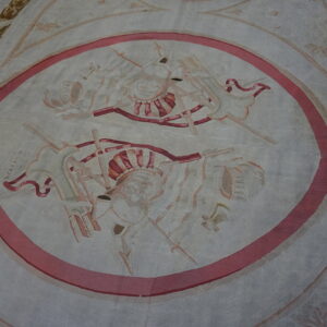 Low-pile cream and grey rug with a central pink-bordered oval containing faded trophy designs.