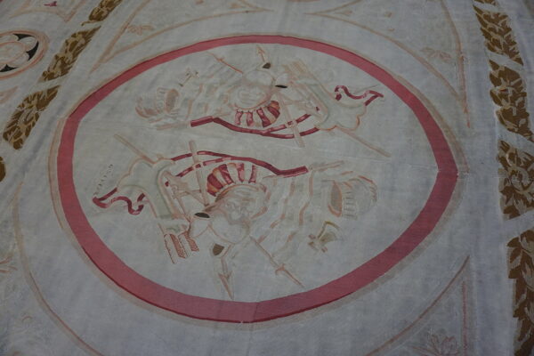 Low-pile cream and grey rug with a central pink-bordered oval containing faded trophy designs.