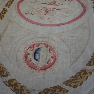 Low-pile rug with a pale ground, ornate pink and blue medallions, and vertical borders of brown and gold leafy garland.