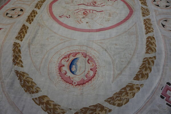 Low-pile rug with a pale ground, ornate pink and blue medallions, and vertical borders of brown and gold leafy garland.