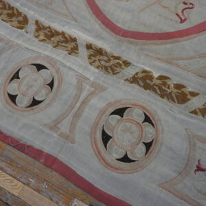 Low-pile blue-gray rug with brown foliage and pink borders on worn wooden floorboards.