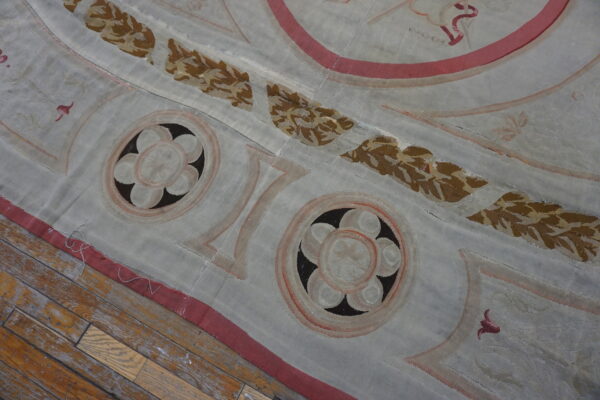 Low-pile blue-gray rug with brown foliage and pink borders on worn wooden floorboards.