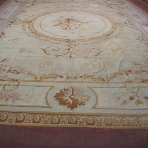 Ornate pale rug with pink flowers and tan scrollwork, surrounded by a deep mauve outer border.