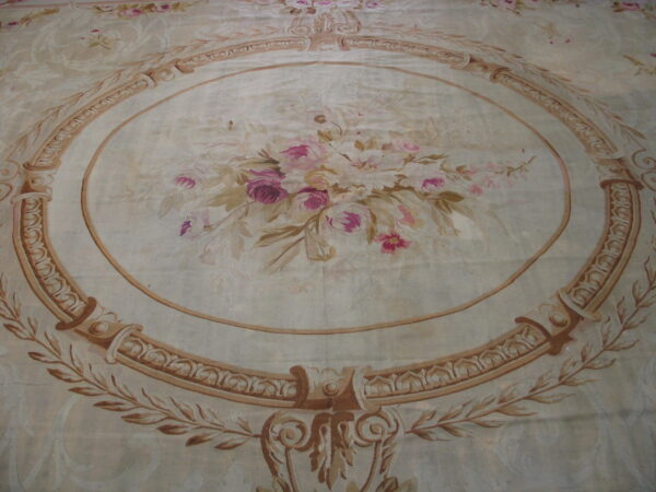 Ornate area rug featuring a pale background, pink floral bouquet, and a thick brown decorative oval border.