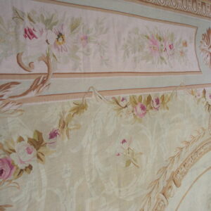 Muted neoclassical rug detail with cream ground, pink florals, green accents, and elaborate tan borders.