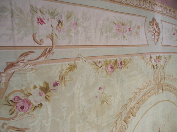 Muted neoclassical rug detail with cream ground, pink florals, green accents, and elaborate tan borders.