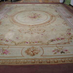 Large low-pile beige rug featuring pink floral sprays, a central medallion, and elaborate tan borders.