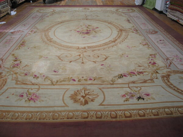 Large low-pile beige rug featuring pink floral sprays, a central medallion, and elaborate tan borders.