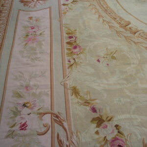 Ornate low-pile rug with pink roses, pale green accents, and large tan scrolling medallions on a cream ground.