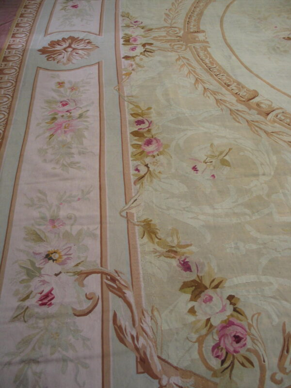 Ornate low-pile rug with pink roses, pale green accents, and large tan scrolling medallions on a cream ground.