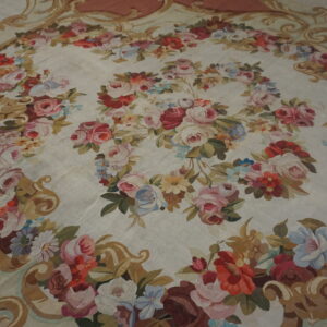 Low-pile cream rug with a dense garland of multicolor roses and an ornate gold and mauve border.