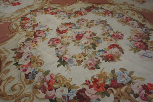 Low-pile cream rug with a dense garland of multicolor roses and an ornate gold and mauve border.