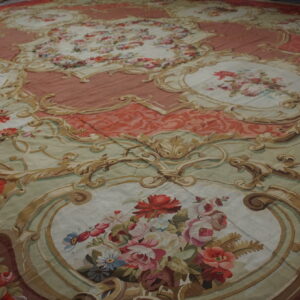 Flatweave rug with pink, sage, and tan rococo scrollwork surrounding detailed floral medallions.