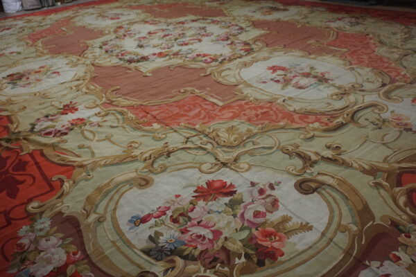 Flatweave rug with pink, sage, and tan rococo scrollwork surrounding detailed floral medallions.