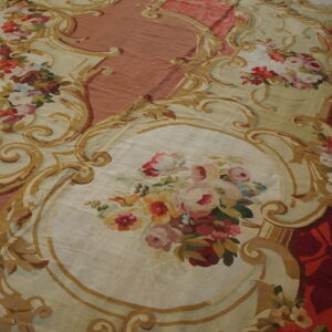Ornate, low-pile rug with elaborate gold scrollwork framing bouquets on cream, set against red and rose fields.