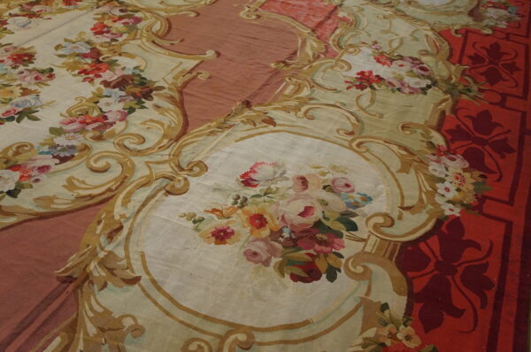 Ornate, low-pile rug with elaborate gold scrollwork framing bouquets on cream, set against red and rose fields.