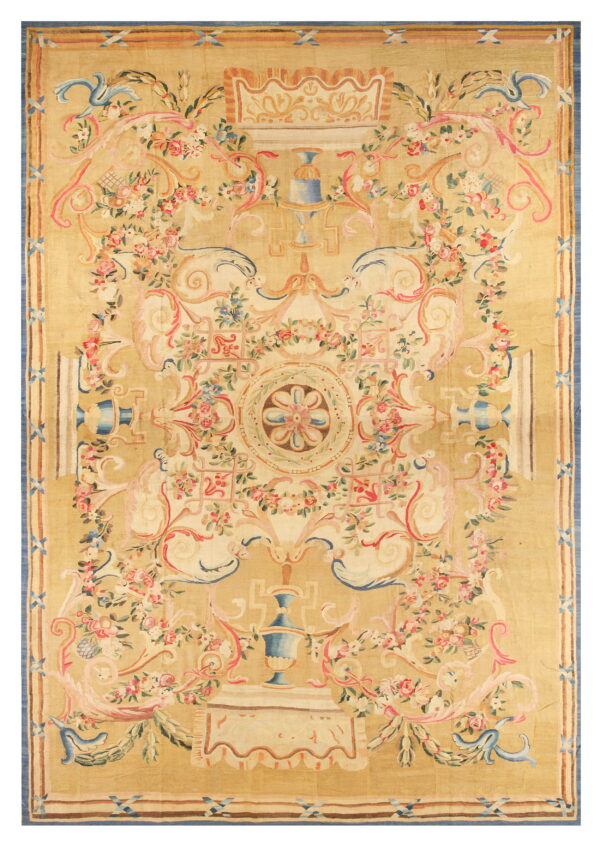 Tan low-pile rug featuring a dense neoclassical design of pink roses, blue urns, and scrolling cream foliage.