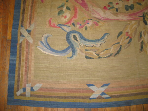 Muted flatweave rug featuring blue scrollwork and pink florals on a beige field, resting on light brown wood planks.