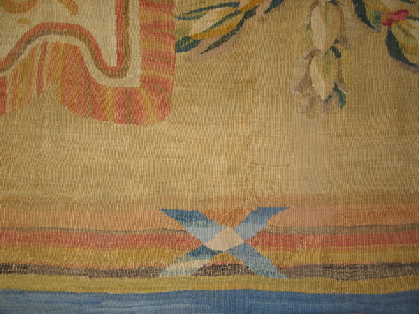 Muted tan textile with terracotta, olive green, and blue geometric patterns over horizontal colored stripes.