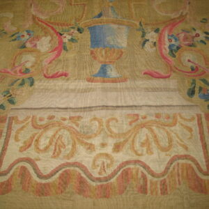 Muted low-pile rug with blue, pink, and green accents in an ornate vase and floral design.