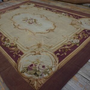 Cream and burgundy rug with ornate floral medallions and gold scrolling borders lies on rustic wooden flooring.