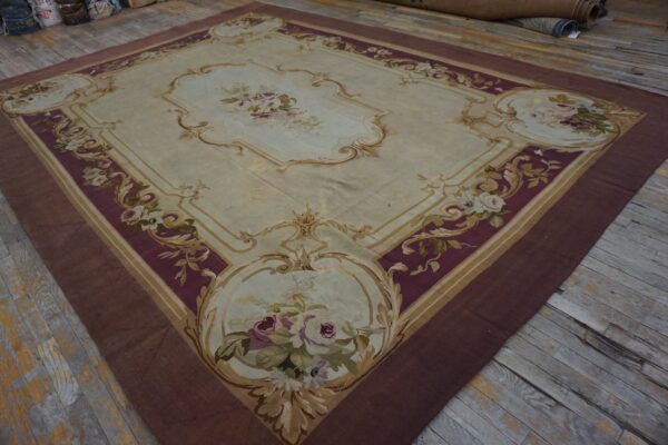 Cream and burgundy rug with ornate floral medallions and gold scrolling borders lies on rustic wooden flooring.