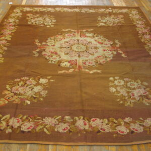 Large, brown flatweave rug with a central cream and pink floral medallion and garland border on wood floor.