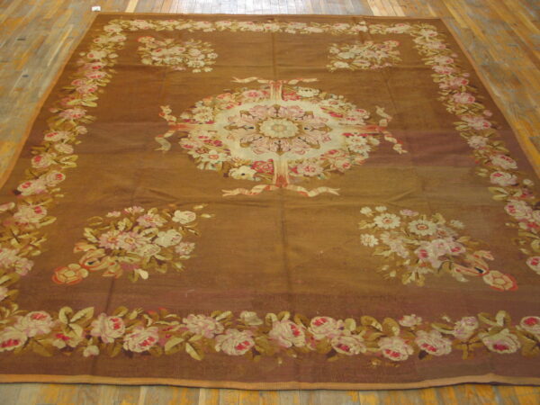Large, brown flatweave rug with a central cream and pink floral medallion and garland border on wood floor.