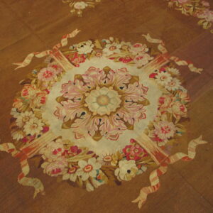 A brown flatwoven rug displays a large central floral medallion detailed with pink, cream, and gold blossoms.