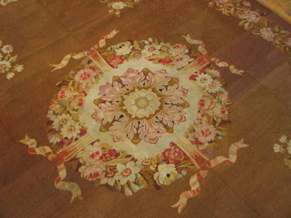 A brown flatwoven rug displays a large central floral medallion detailed with pink, cream, and gold blossoms.
