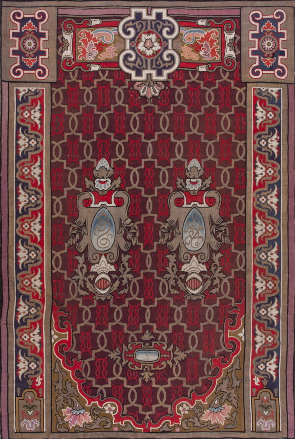 An ornate red and gray rug with a geometric lattice center and colorful symmetrical shield motifs.
