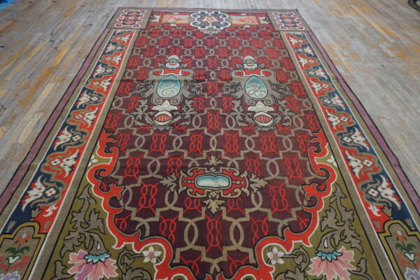 Ornate low-pile rug with a maroon and red geometric field, colorful borders, placed on distressed wood planking.