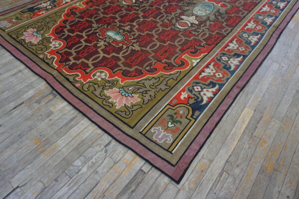 Ornate flatweave rug featuring a maroon geometric field and borders of olive green and navy blue on distressed gray wood.