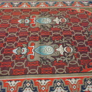 Ornate low-pile rug with maroon, red, gold, and blue motifs over a geometric chain pattern.