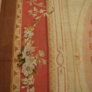 Woven rug detail showing vertical bands of brown, red florals, and beige ornamental scrollwork on wood planks.