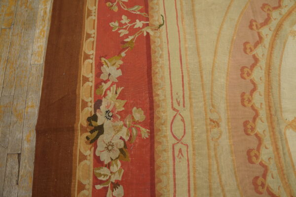 Woven rug detail showing vertical bands of brown, red florals, and beige ornamental scrollwork on wood planks.